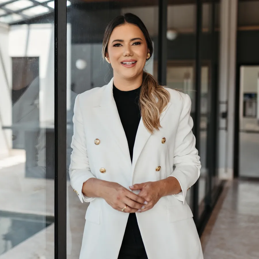 Dra. Fabiana Amaro, de blazer branco, sorrindo no ambiente da clínica